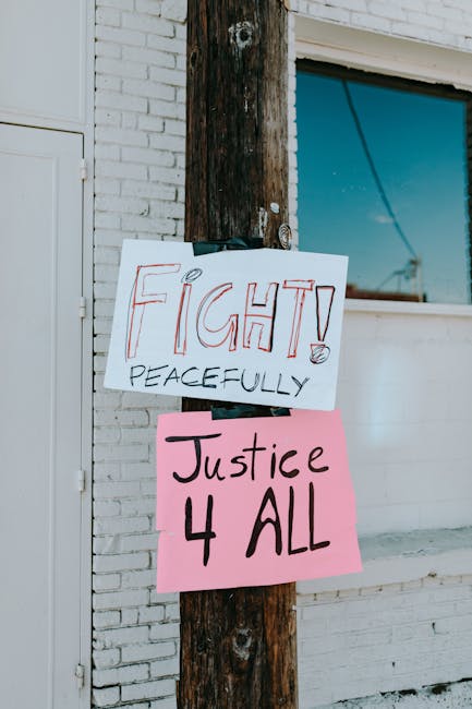 Protest signs advocating justice and peaceful activism attached to a street pole outdoors.