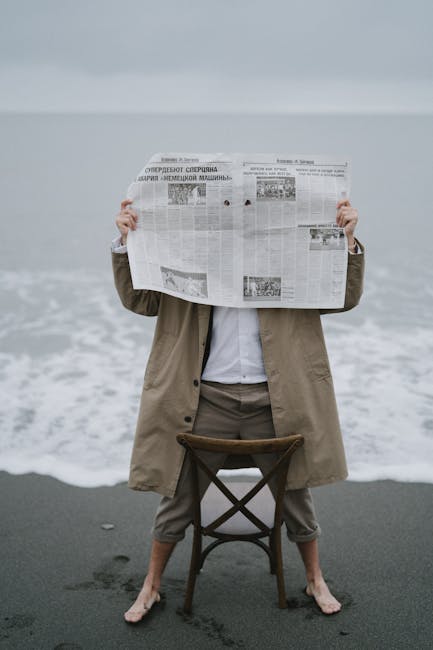 Adult holding newspaper while standing on beach, creating a serene oceanfront scene.