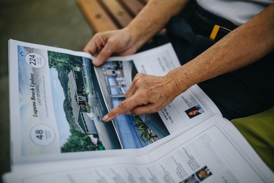 A senior adult's hands holding and reading a newspaper while seated on an outdoor bench.