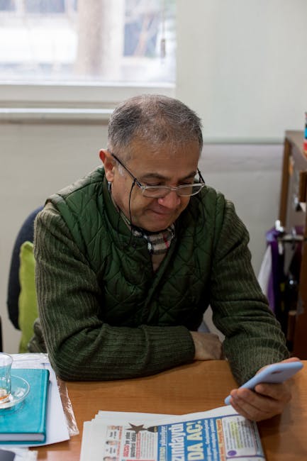 A middle-aged man focused on reading news on his smartphone at a workplace indoors.